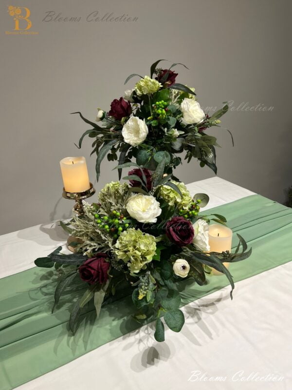 Plum Floral Arrangement by Blooms Collection: A captivating fusion of roses, berries, hydrangeas, eucalyptus, and greens. Versatile centerpiece or aisle decoration, perfect for weddings or special events. Premium artificial flowers ensure lifelike allure.